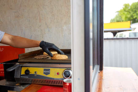 Chef cooking a cutlet and a bun on grill for perfect burger in a street cart. Street food market vendor. Delicious cheese burger. Outdoor meal. Quick snack for busy ones. Nutritious junk food. Fast food concept.の写真素材