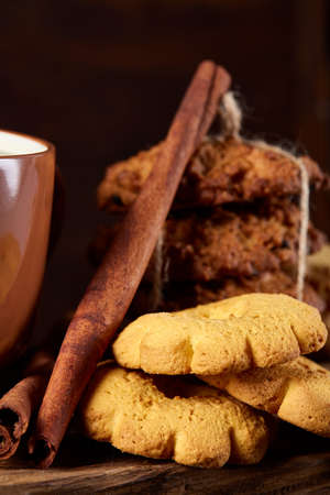 Sweet Christmas teatime with oatmeal, chocolate biscuits, cinnamon sticks and dried oranges, on rustic wooden background, close-up, selective focus. Christmas concept. Festive background.の写真素材