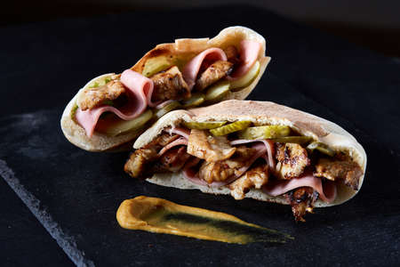Stuffed pita bread with pork chops, grilled vegetables and sauce on black stony background, close-up, selective focus, vertical. Organic stuffed roll for delicious lunch. Traditional Middle East cuisine. Fast food concept.の写真素材