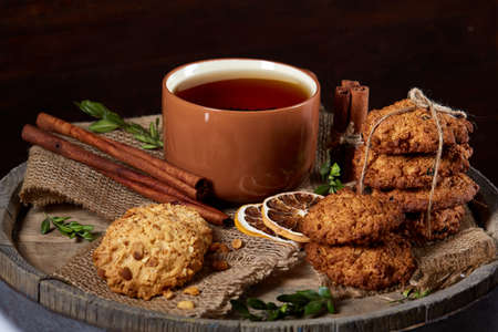 Sweet Christmas teatime with oatmeal, chocolate biscuits, cinnamon sticks and dried oranges, on rustic wooden background, close-up, selective focus. Christmas concept. Festive background.の写真素材