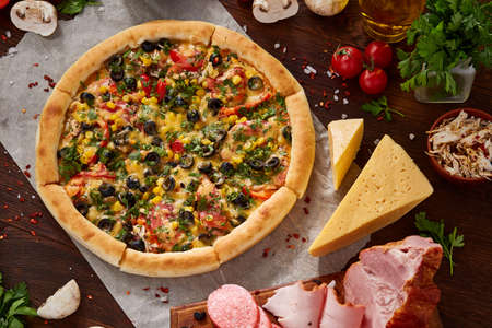Pizza still life. Freshly baked Italian pizza and its components arranged on wooden background, top view, close-up, selective focus. Delicious snack. Traditional homemade Italian pizza. Mediterranian cuisine. Fast food concept.の写真素材