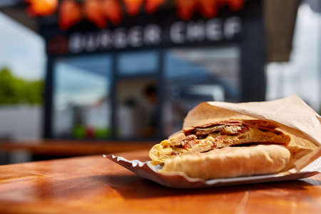 First person view shot of a man eating hamburger in the street cafe, soft focus, shallow depth of field. Yummy snack on the urban background. Delicious outdoor lunch in the open air cafe. Street food concept. Fast food concept.の写真素材