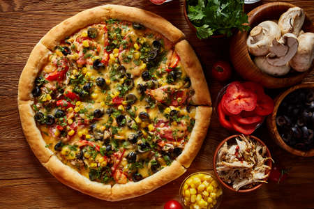Pizza still life. Part of freshly baked Italian pizza and its components arranged on wooden background, top view, close-up, selective focus. Delicious snack. Traditional homemade Italian pizza. Mediterranian cuisine. Fast food concept.の写真素材