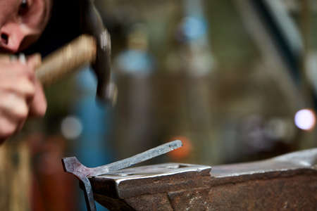 Close-up of a blacksmiths hands manipulating a metal piece above his forge, selective focus.