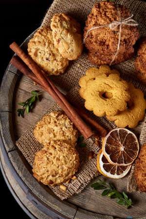 Conceptual composition with assortment of cookies, cinnamon sticks bunch and dried oranges with burlap napkin on a wooden barrel over rustic background, selective focus, close-up. Delicious treat. Relaxing teatime. Christmas background.の写真素材