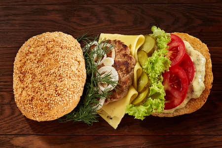 Close-up of delicious fresh home made burger with piccoli, lettuce, cheese, onion, tomato, dill and yummy beef on a dark wooden background. Traditional American hamburger. Junk food full of calories. Fast food concept.の写真素材