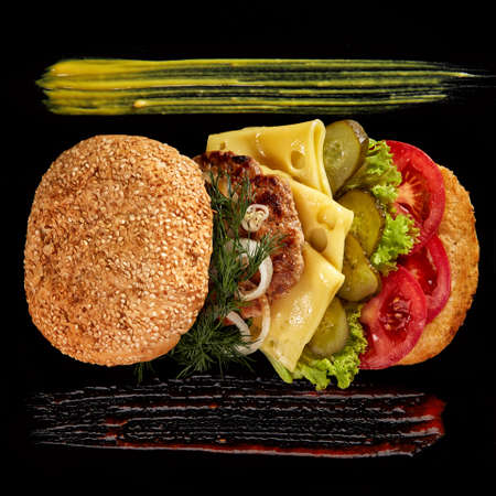 Big fresh burger with sauce arranged on black square plate on black wooden background, flat lay, close-up, selective focus. American classic burger menu. Artistic serving. Nutritious junk food. Fast food concept.の写真素材