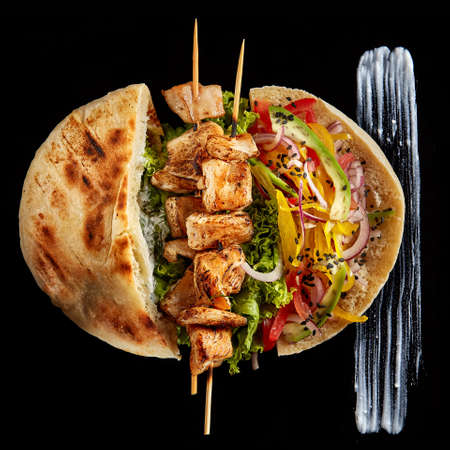 Tasty Jewish pita stuffed with grilled chicken, vegetables, letucce and kebab on vintage wooden background, top view, close-up, shallow depth of field, blurred. Organic roll for delicious lunch. Traditional Middle East cuisine. Fast food concept.の写真素材