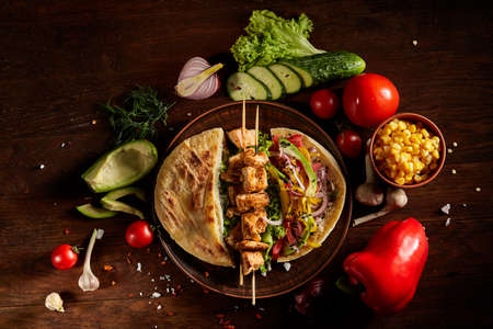 Exotic still slife with pita on an old-fashioned plate, fresh vegetables and yummy kebab over vintage wooden background, top view, close-up, selective focus. Mediterranian or Middle East cuisine. Rustic food background. Fast food concept.の写真素材