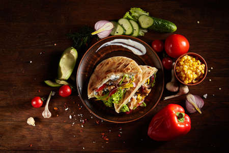 Exotic still slife with pita on an old-fashioned plate, fresh vegetables and yummy kebab over vintage wooden background, top view, close-up, selective focus. Mediterranian or Middle East cuisine. Rustic food background. Fast food concept.の写真素材