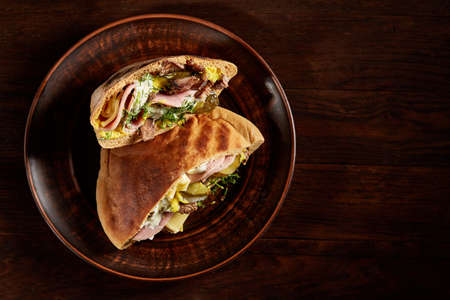Tasty Jewish pita stuffed with grilled meat, ham, cheese, piccoli and sauce on vintage wooden background, top view, close-up, selective focus. Organic stuffed roll for delicious lunch. Traditional Middle East cuisine. Fast food concept.の写真素材