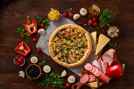 Pizza still life. Freshly baked Italian pizza and its components arranged on wooden background, top view, close-up, selective focus. Delicious snack. Traditional homemade Italian pizza. Mediterranian cuisine. Fast food concept.の写真素材