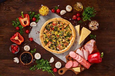 Pizza still life. Freshly baked Italian pizza and its components arranged on wooden background, top view, close-up, selective focus. Delicious snack. Traditional homemade Italian pizza. Mediterranian cuisine. Fast food concept.の写真素材
