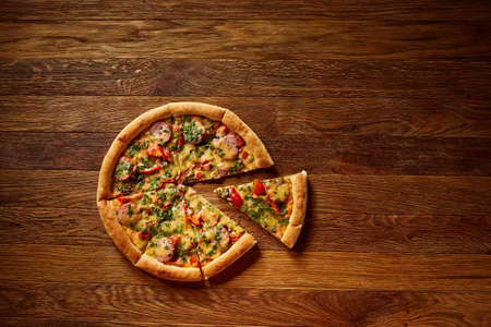Freshly baked delicious pizza divided into slices on rustic wooden background, top view, close-up, selective focus. Some copy space for your text. Delicious snack. Yummy junk food. Traditional Italian pizza. Mediterranian cuisine. Fast food concept.の写真素材