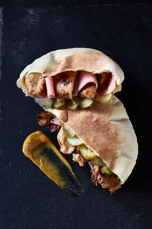 Stuffed pita bread with grilled vegetables and chiken chops on black stony background.の写真素材