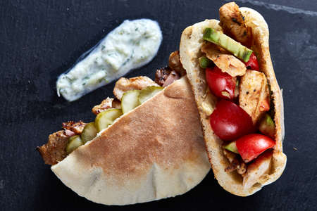 Stuffed pita bread with pork chops, grilled vegetables and sauce on black stony background, close-up, selective focus, vertical. Organic stuffed roll for delicious lunch. Traditional Middle East cuisine. Fast food concept.の写真素材