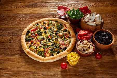 Pizza still life. Freshly baked Italian pizza and its components arranged on wooden background, top view, close-up, selective focus. Delicious snack. Traditional homemade Italian pizza. Mediterranian cuisine. Fast food concept.の写真素材