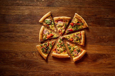 Freshly baked delicious pizza divided into slices on rustic wooden background, top view, close-up, selective focus. Some copy space for your text. Delicious snack. Yummy junk food. Traditional Italian pizza. Mediterranian cuisine. Fast food concept.の写真素材