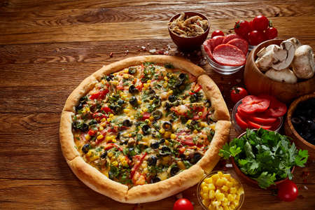 Pizza still life. Freshly baked Italian pizza and its components arranged on wooden background, top view, close-up, selective focus. Delicious snack. Traditional homemade Italian pizza. Mediterranian cuisine. Fast food concept.の写真素材