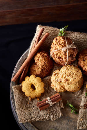 Conceptual composition with assortment of cookies, cinnamon sticks bunch and dried oranges with burlap napkin on a wooden barrel over rustic background, selective focus, close-up. Delicious treat. Relaxing teatime. Christmas background.の写真素材