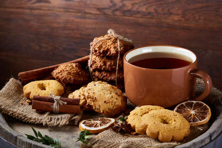 Sweet Christmas teatime with oatmeal, chocolate biscuits, cinnamon sticks and dried oranges, on rustic wooden background, close-up, selective focus. Christmas concept. Festive background.の写真素材