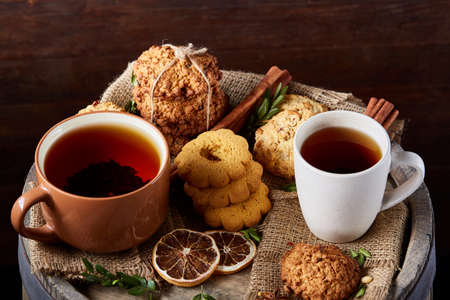 Sweet Christmas teatime with oatmeal, chocolate biscuits, cinnamon sticks and dried oranges, on rustic wooden background, close-up, selective focus. Christmas concept. Festive background.の写真素材