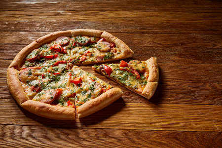 Freshly baked delicious pizza divided into slices on rustic wooden background, top view, close-up, selective focus. Some copy space for your text. Delicious snack. Yummy junk food. Traditional Italian pizza. Mediterranian cuisine. Fast food concept.の写真素材