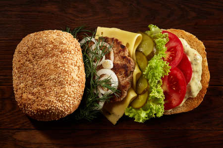 Close-up of delicious fresh home made burger with piccoli, lettuce, cheese, onion, tomato, dill and yummy beef on a dark wooden background. Traditional American hamburger. Junk food full of calories. Fast food concept.の写真素材