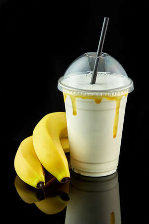 Health food. Plastic cup of milkshake with banana isolated on balck backgroundの写真素材