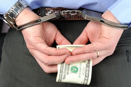 Man in handcuffs holds banknotes in his palms behind his back