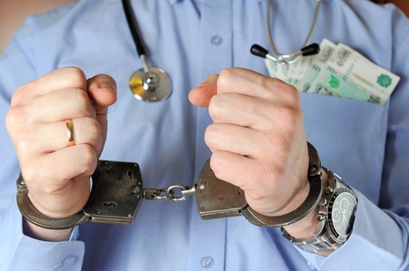 Man with stethoscope holds his hands in handcuffs before itself with money in the pocket