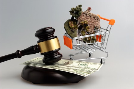 Hammer of judge with dollars and model of house in trolley on gray backgroundの写真素材