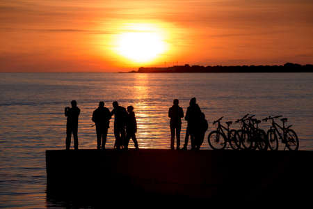 Silhouettes of people walking on the pier against the sea and the Golden sunsetの写真素材