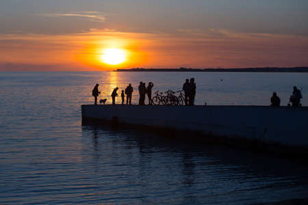 Silhouettes of people walking on the pier against the sea and the Golden sunsetの写真素材