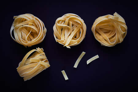 Dry Italian pasta tagliatelle nest against a dark background
