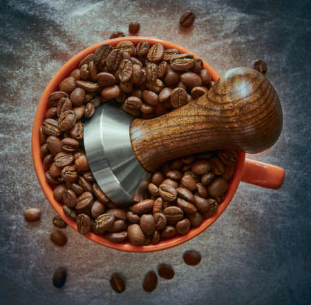 Coffee tamper in a cup with coffee beans on a silver backgroundの写真素材