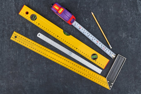 Ruler, tape measure, construction level and pencil on gray background, close-up view from above
