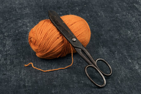Old rusty tailor scissors and a tangle of orange color woolen yarn in close-up