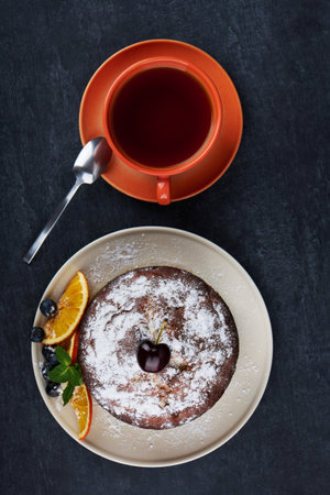 Delicious fruity cake in plate with slices of dried orange and a cup of tea on dark table background, closeup, top viewの写真素材