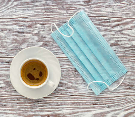 Coffee cup and medical mask on wooden table in cafe, concept of life in a pandemic, flat layの写真素材