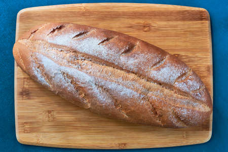 Loaf of freshly baked white bread on a wooden board close up