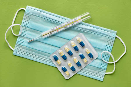 Thermometer and the blister with the capsules are on the medical mask, close up