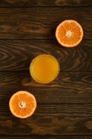 Juicy mandarin halves and a glass of juice arranged diagonally on a wooden backgroundの写真素材