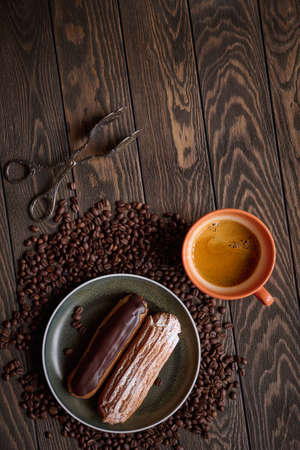Top view of two French eclairs and a cup of espresso coffee on a wooden table against a scattering of coffee beans, top view with copy spaceの写真素材