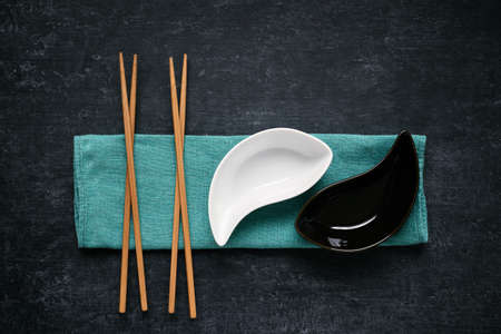 Black and white ceramic bowls and chopsticks lying on linen napkin, dark background, top viewの写真素材