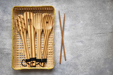 Set of wooden bamboo kitchen utensils in wicker basket on gray background with copy space, top viewの写真素材
