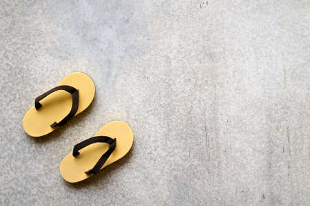 Tiny decorative flip-flops on gray concrete background close-up with space for textの写真素材