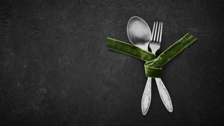 Spoon and fork tied with green velvet ribbon on black background