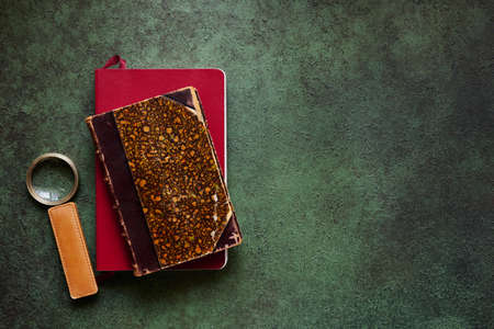 Magnifying glass with leather handle and old books on textured green background, top view