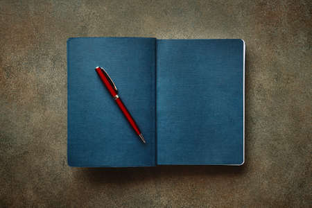 Beautiful red fountain pen rests on textured blue diary, close-up, stylized